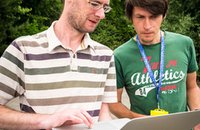 Teacher and engineer collaborating with racing car data on a laptop