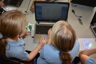 3 children testing lights under paper in front of laptop
